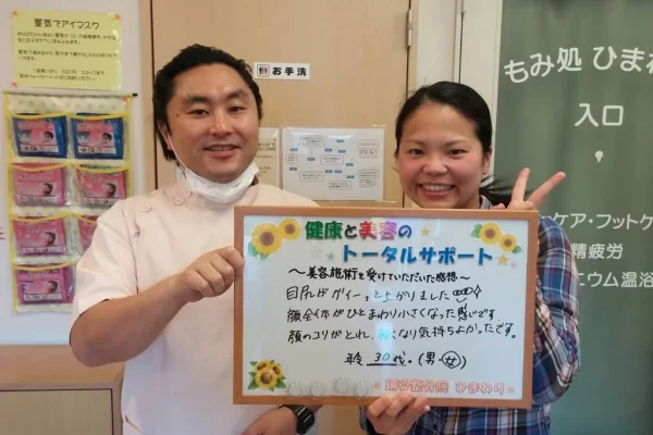 横須賀市の鍼灸整骨院ひまわり北久里浜院で、美容鍼の施術を受け、「目元がグイーっと上がりました」と書かれたボードを掲げる施術者と患者様の様子。