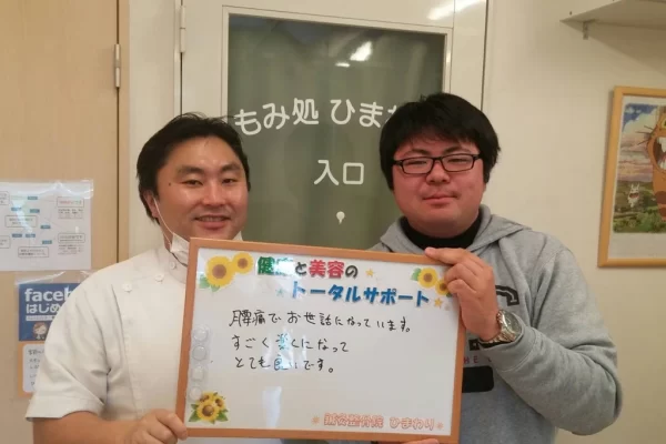 横須賀市の鍼灸整骨院ひまわり北久里浜院で、腰痛が改善し「とても良いです」と書かれたボードを掲げる施術者と患者様の様子。