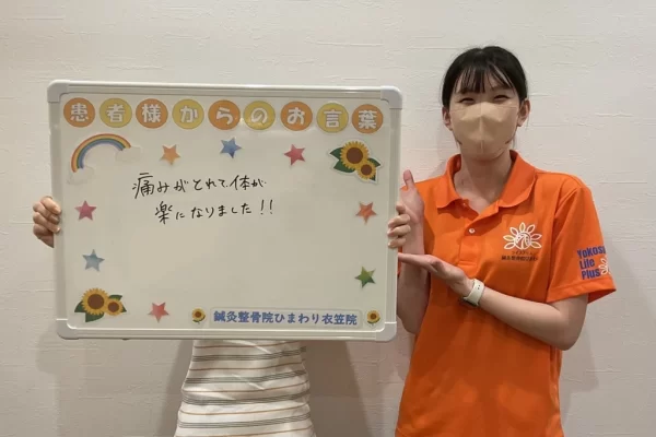 横須賀市の鍼灸整骨院ひまわり衣笠院に寄せられた、20代女性の患者様の声。「首・肩の痛みがとれて体が楽になりました!!」と書かれたボードを掲げるスタッフ。