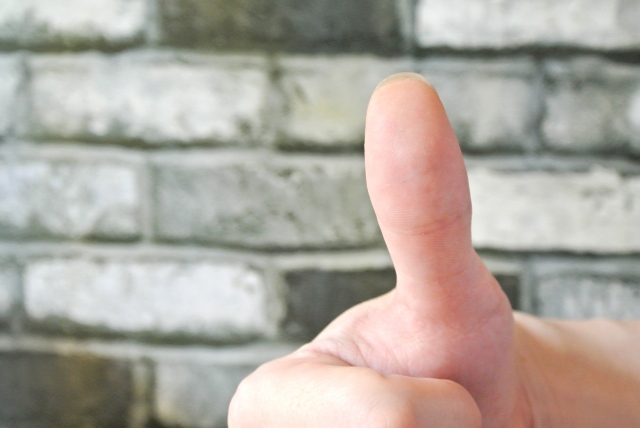 親指を立てて「いいね」のサインをしている手のクローズアップ。背景はレンガ模様の壁。