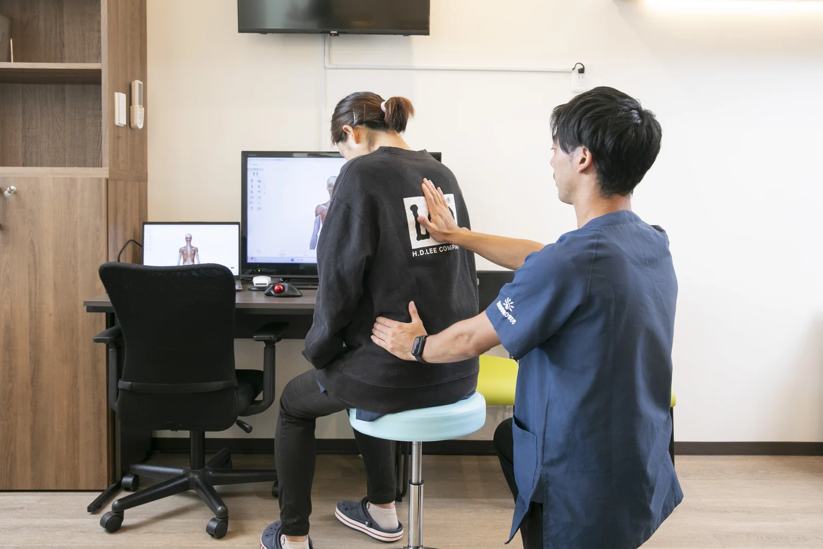 椅子に座った方の背中と腰に手を添えて体の状態を確認するスタッフ