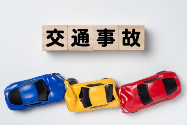 自動車事故:ミニカーで見る交通事故の状況 「交通事故」と書かれた木製ブロックと、横転している青、黄、赤の車のミニカー。