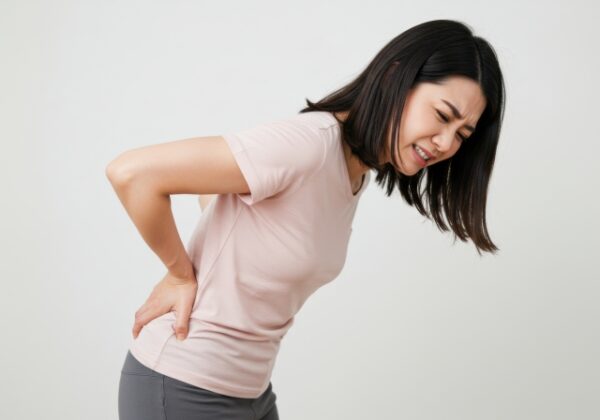 ピンクのTシャツとグレーのパンツを着用した女性が、腰を抑えて痛みに顔をゆがめている。