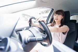 運転席に座り、ハンドルを握って驚いたような表情をしている女性。