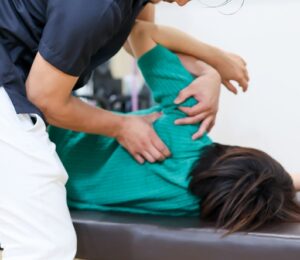 施術ベッドで横になった患者の肩関節に対して施術を行う様子。回旋腱板損傷の治療イメージ。