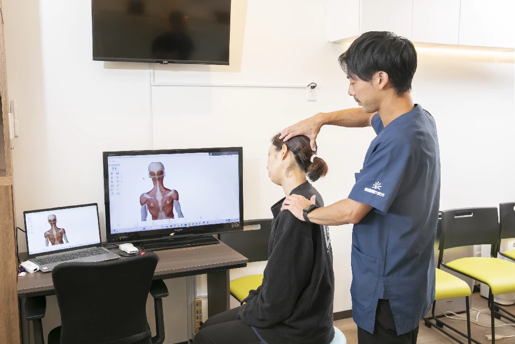 横須賀市の鍼灸整骨院ひまわり（北久里浜院・衣笠院）で行う、むちうち施術の検査・カウンセリング。施術者が患者様の首（頚椎）の状態を触診し、モニターで筋肉の状態を説明している様子。