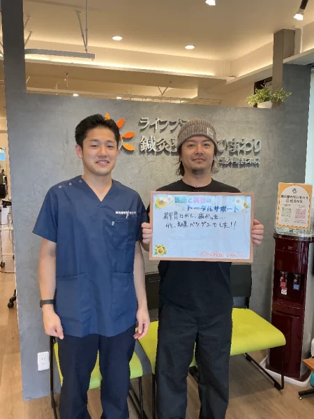 横須賀市・北久里浜|肩甲骨はがしで肩こり改善なら鍼灸整骨院ひまわり北久里浜院 北久里浜院の受付前で患者さまとスタッフが記念撮影。ボードに「肩甲骨はがし、痛かった…けど、効果抜群でした!」のメッセージ