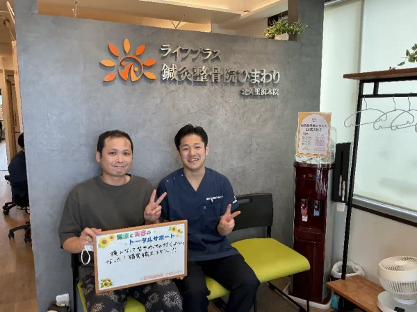 北久里浜院の待合で患者様と施術者がボードを掲示。「横になって背中がめっちゃつくようになった。猫背矯正すげー。」という感想入りの写真