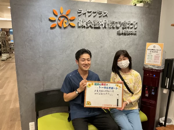 北久里浜院の待合で患者様と施術者がボードを掲げた写真。「大変気持ちが良かったです。体がスッキリしました。」の感想入り