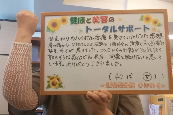 横須賀市の鍼灸整骨院ひまわり北久里浜院で、ハイボルテージ施術を受け、「肩の痛みも、ひねってしまった右腕もスッ!!と楽になり、辛さが減りました」と手書きされたボードを掲げる患者様。