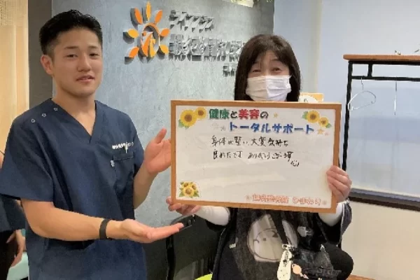 横須賀市の鍼灸整骨院ひまわり北久里浜院で、骨盤矯正プログラムを受け、「体が軽い 大変気持ち良かった」と書かれたボードを掲げる施術者と患者様の様子。