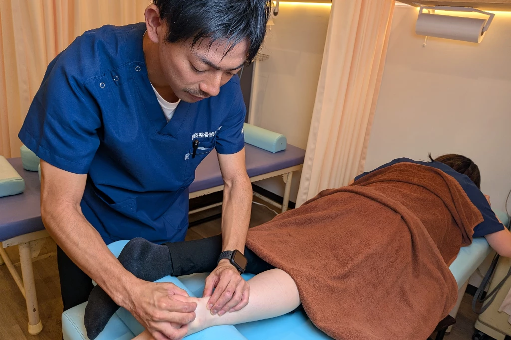 横須賀市の鍼灸整骨院ひまわりで、施術者がアキレス腱炎で痛むふくらはぎとアキレス腱周辺に手技施術を行っている様子