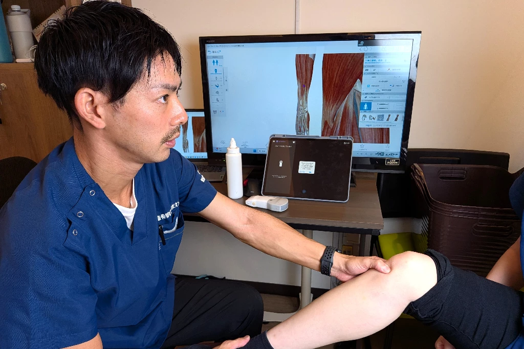 横須賀市の鍼灸整骨院ひまわりで、施術者がジャンパー膝の患者の膝を専門機器と解剖図を見ながら検査している様子