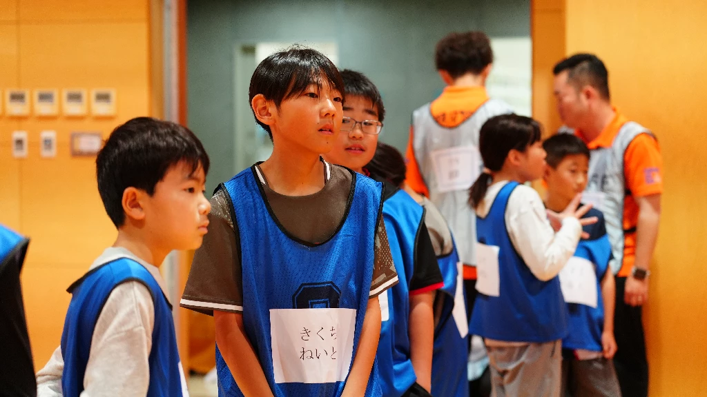 横須賀市のかけっこ教室で、ビブスを着用した参加者の子どもたちが説明を聞きながら並ぶ様子