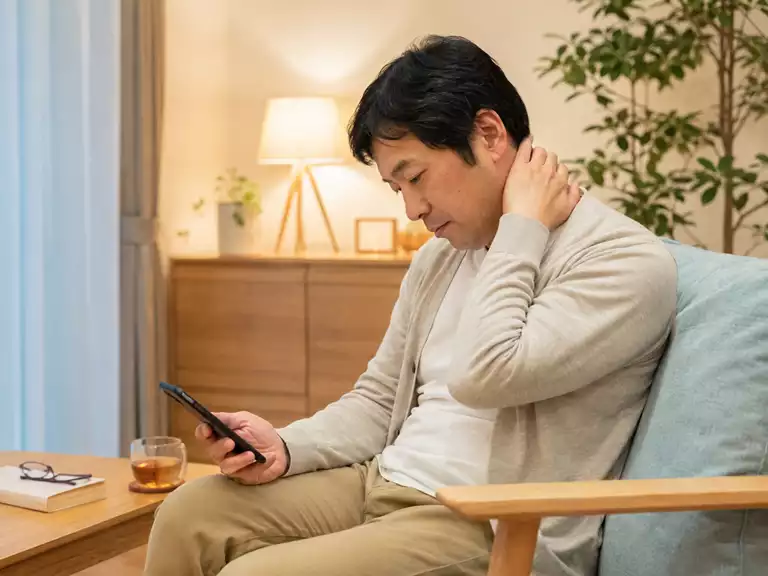 低い位置のスマートフォンを見続ける生活場面 スマホで首がつらい方が低い位置の端末を見て首の後ろに重さを感じている様子