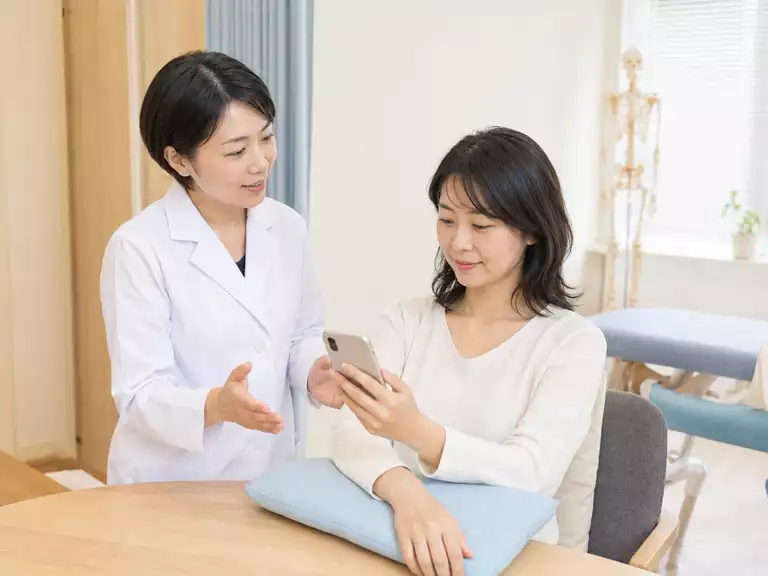 スマートフォンを見る高さと前腕の支え方を確認する場面 スマホで首がつらい方へ施術者が目線の高さと腕の支え方を説明している様子